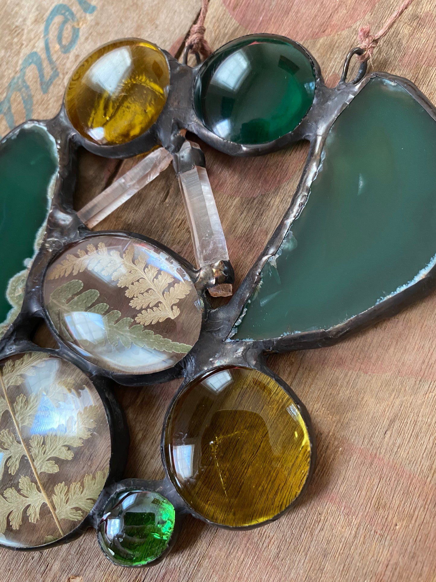 Decorative glass piece with green, gold, and brown colors and ferns agate slices and quartz crystals on a wooden surface.