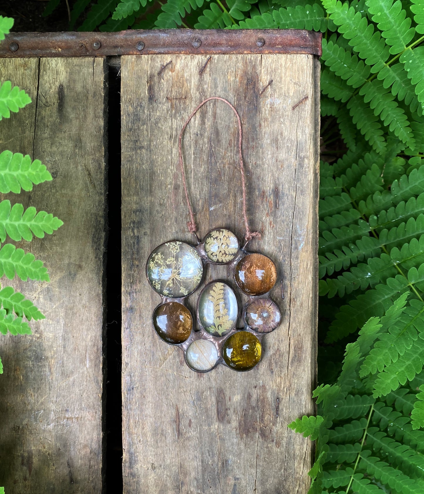 Glass art with pressed flowers and ferns on a wooden block surrounded by ferns.
