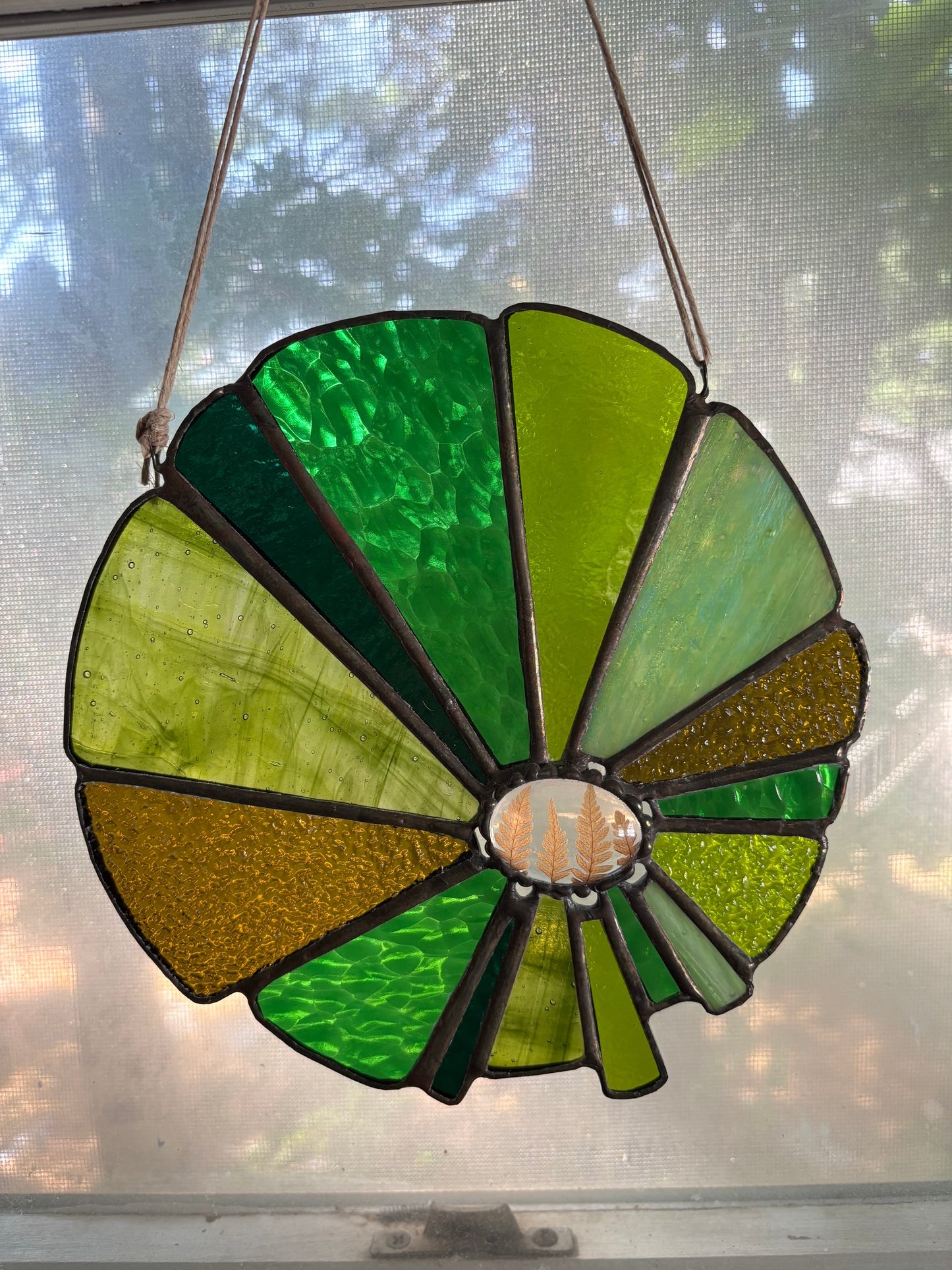 Stained glass sun catcher with green and brown colors in a window.