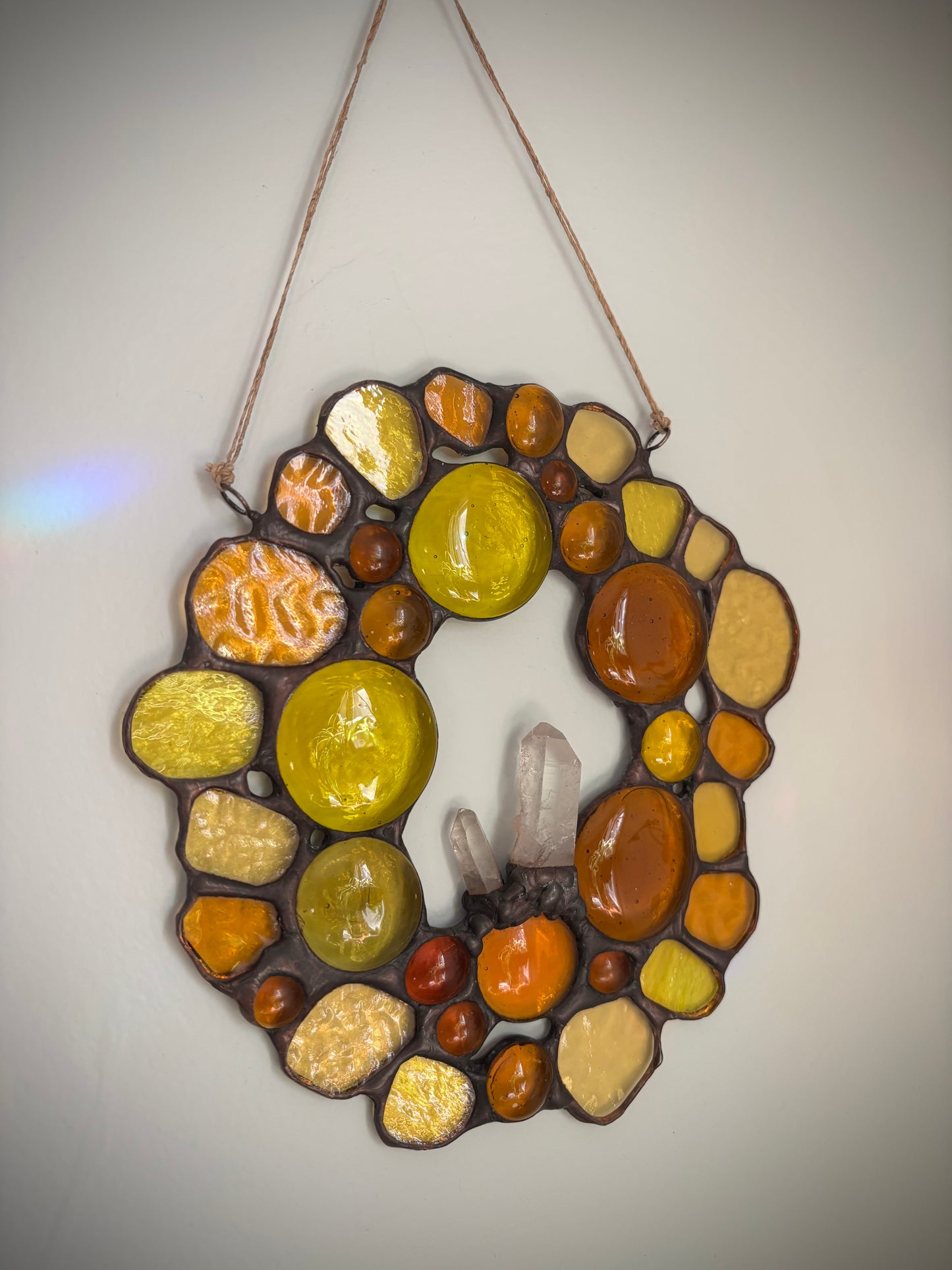 Stained glass suncatcher with autumn colors and quartz crystals on a plain background.