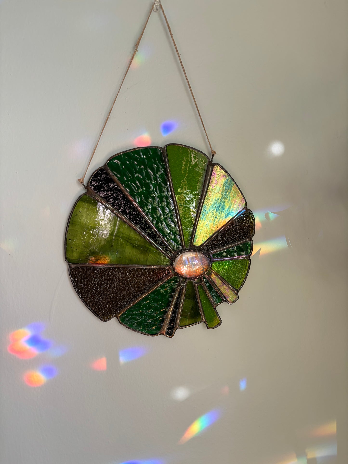 Stained glass sunflower design with greens and pressed ferns on a white background.