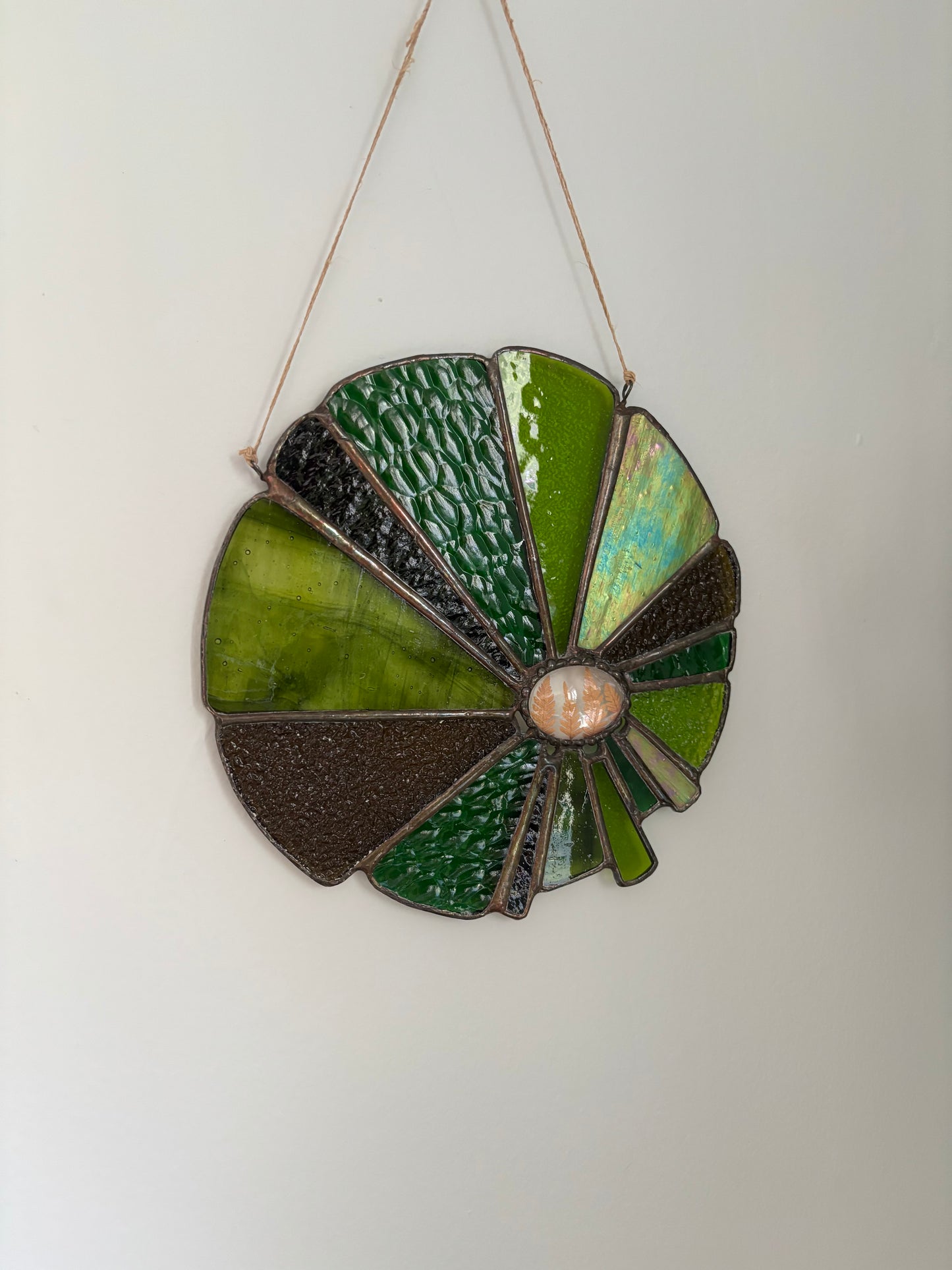 Decorative sun-shaped object with green and brown colors and pressed ferns on a white background.