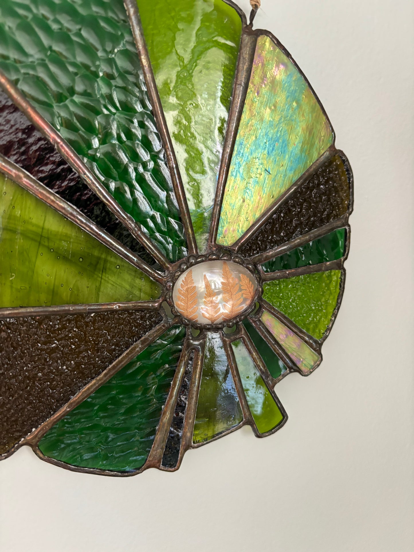 Stained glass panel with green and brown colors and pressed ferns on a white background.
