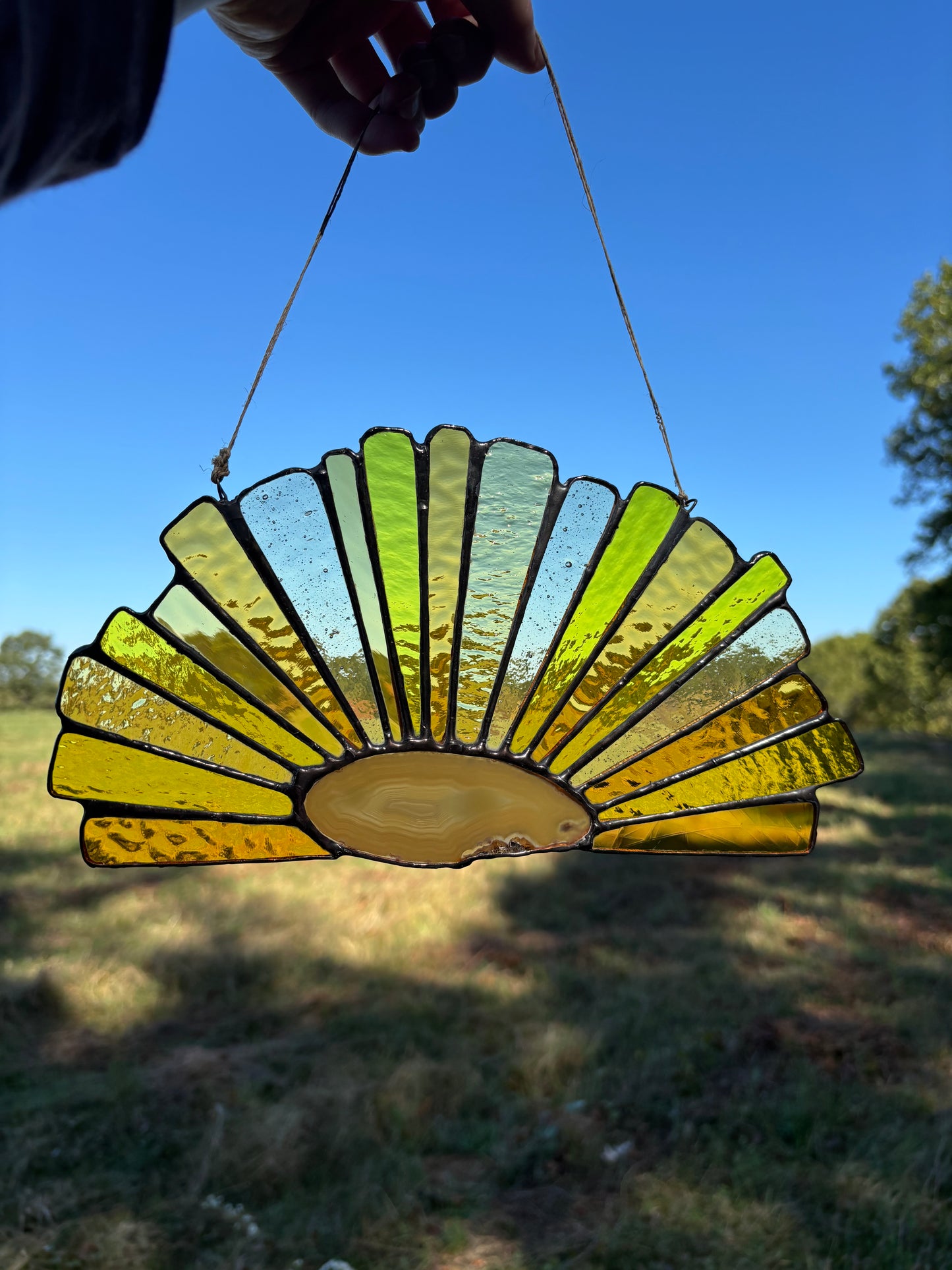 Decorative stained glass with an agate slice hanging outdoors against a blue sky.