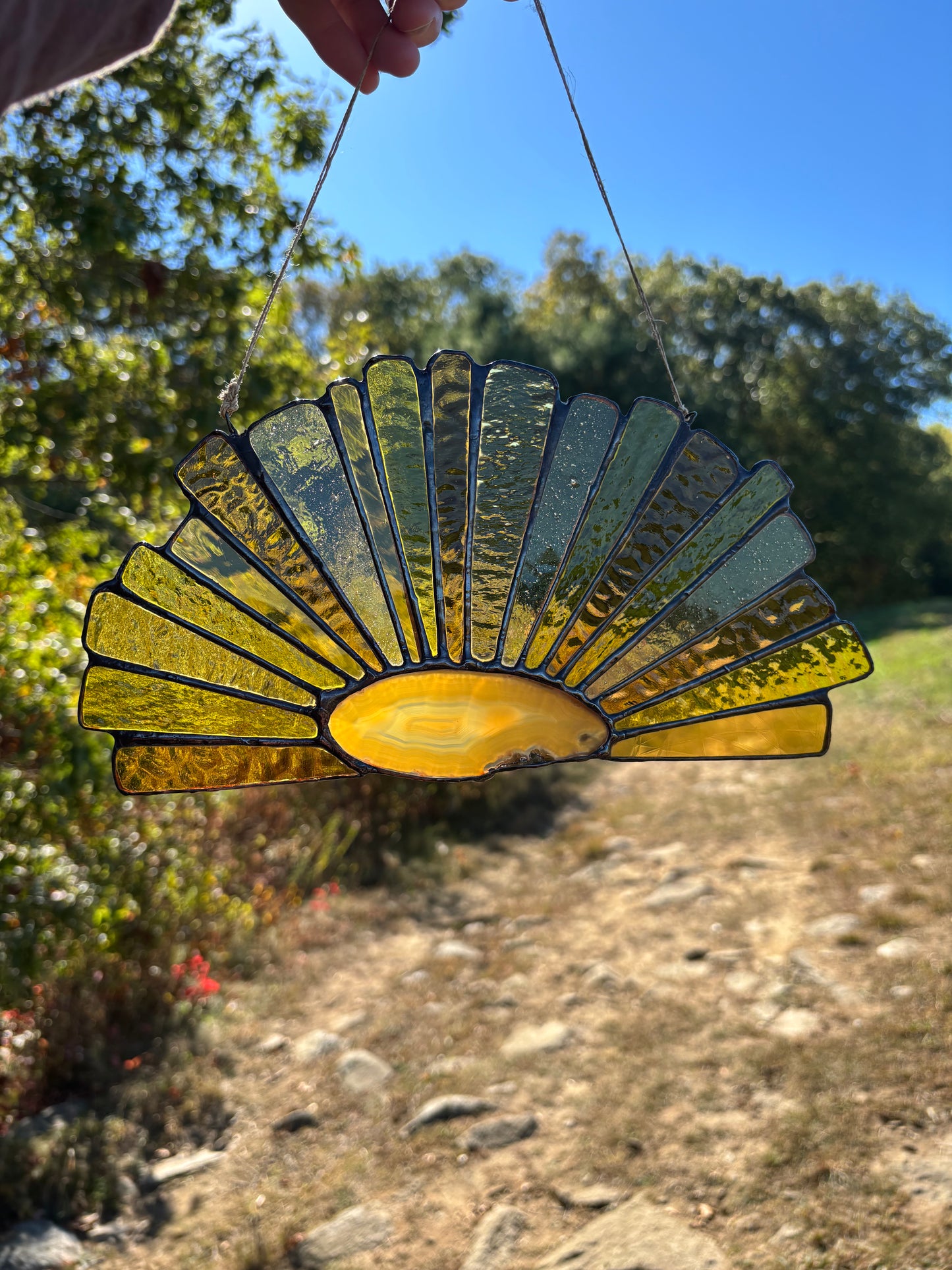 Decorative glass sun catcher with an agate center and yellow rays held against a natural background.
