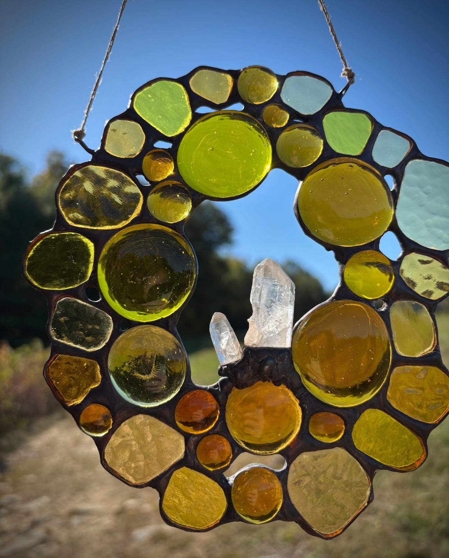 Decorative glass sun catcher with colorful glass pieces and a crystal, set against a natural background.