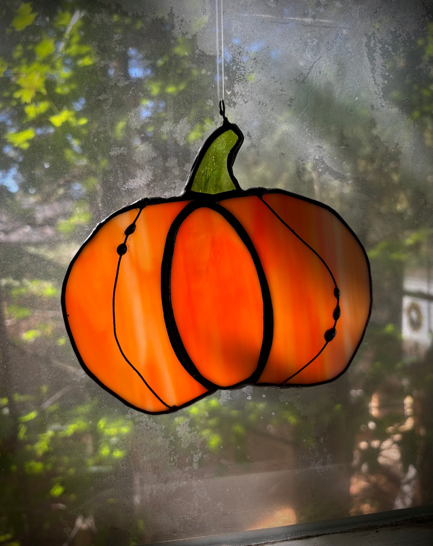 Stained glass pumpkin hanging on a window with a blurred outdoor background.