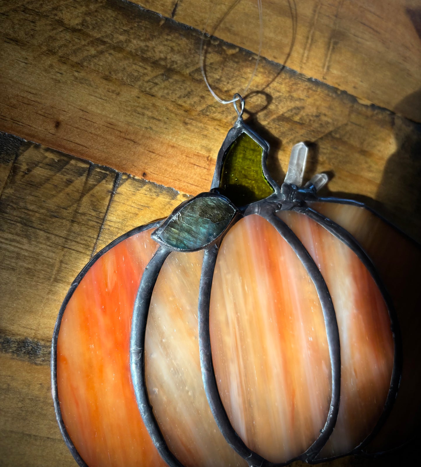 Stained glass pumpkin with quartz crystals and labradorite stone hanging on a wooden surface.