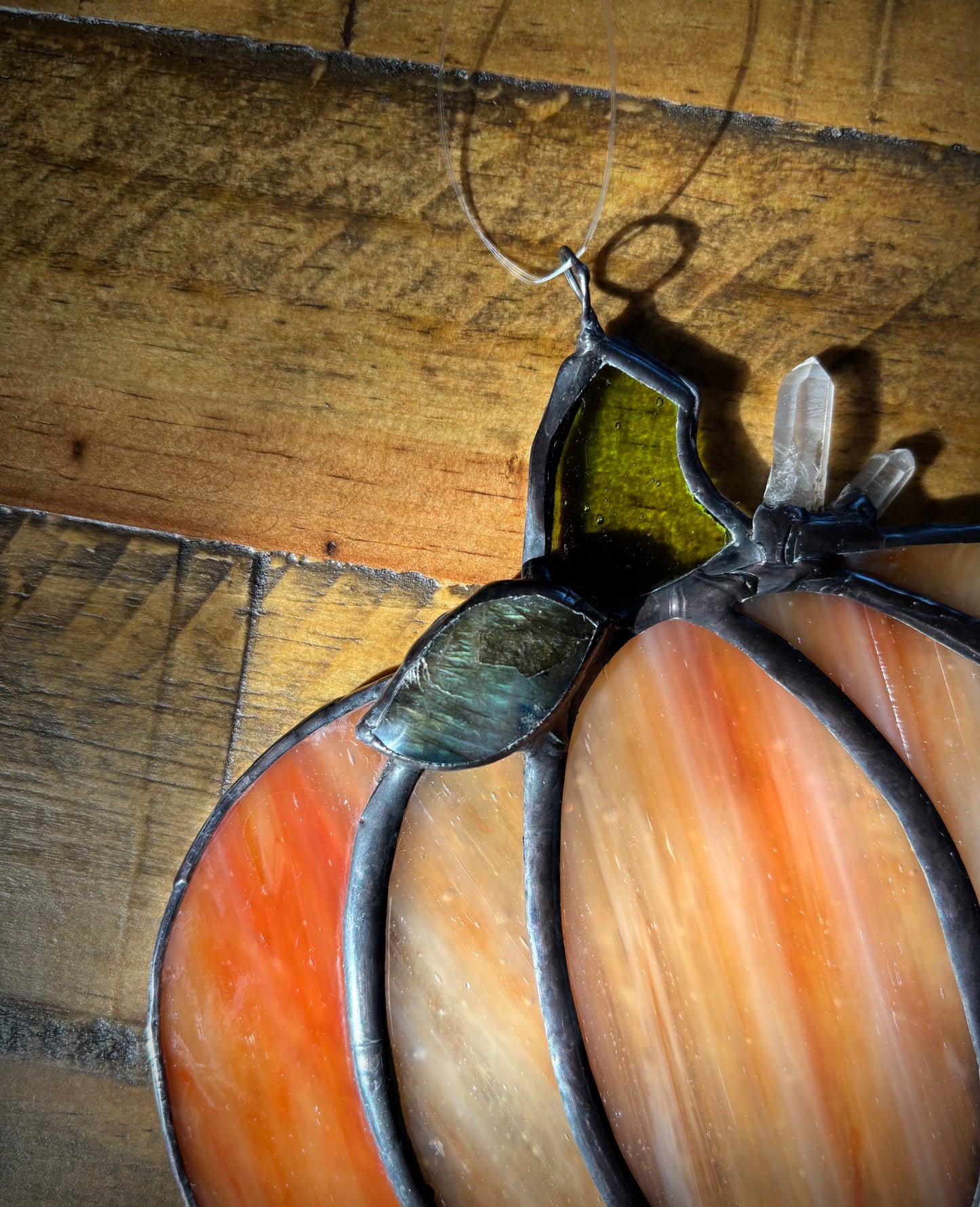 Close-up of a stained glass window panel with a labradorite stone and quartz crystals on a wooden background.