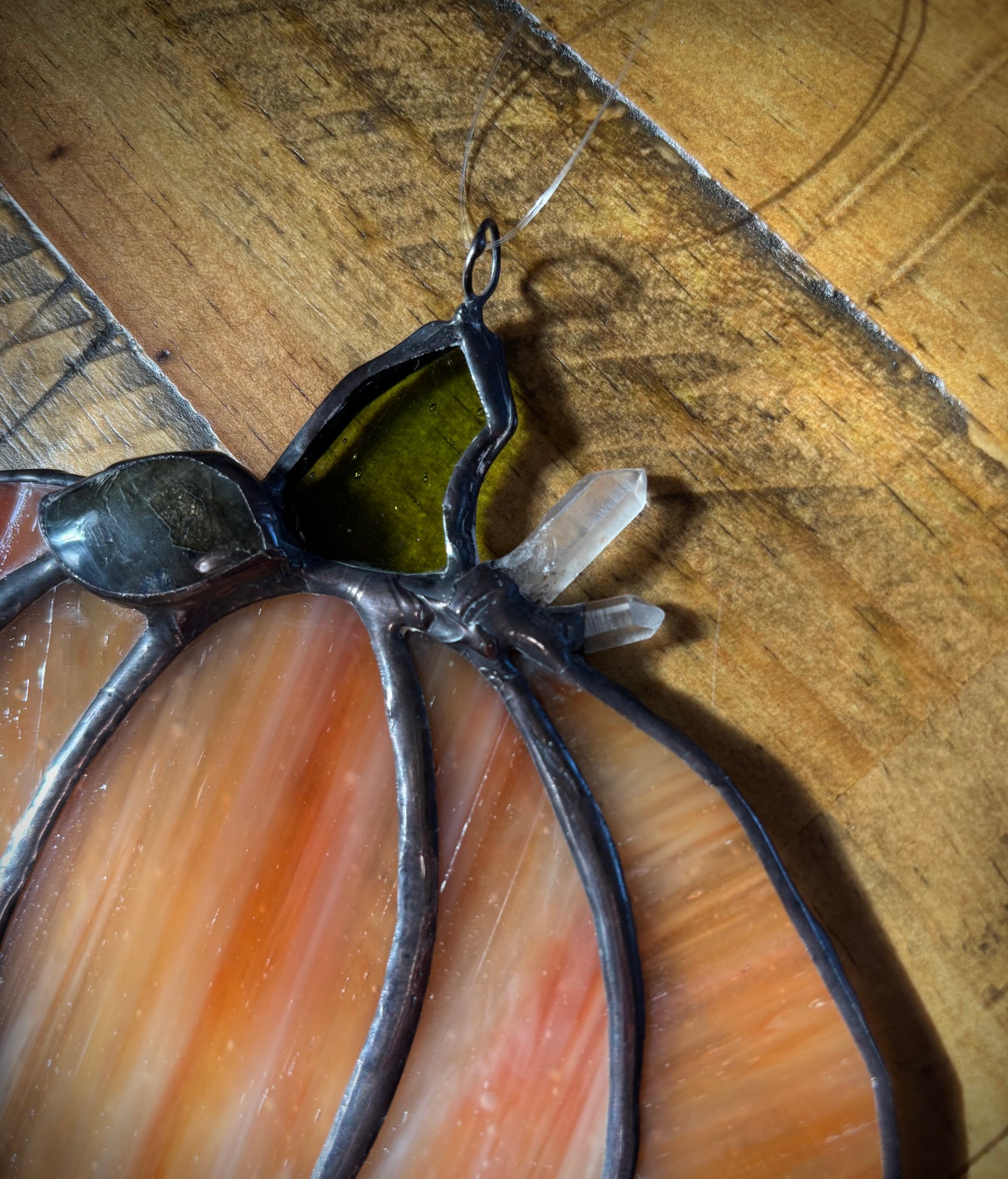 Close up of a stained glass pumpkin with quartz crystals on a wooden background.