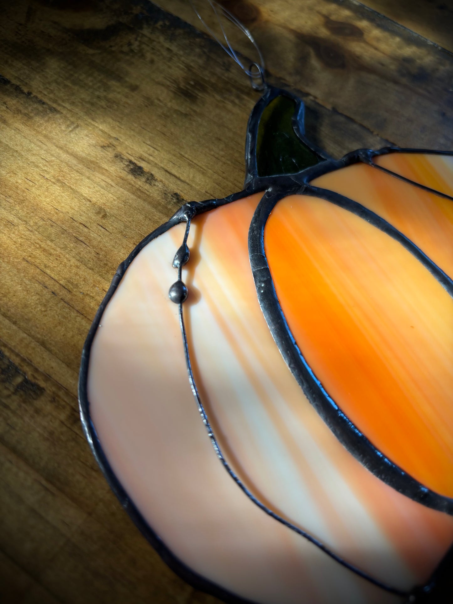 Close up of a stained glass pumpkin on a wooden surface.