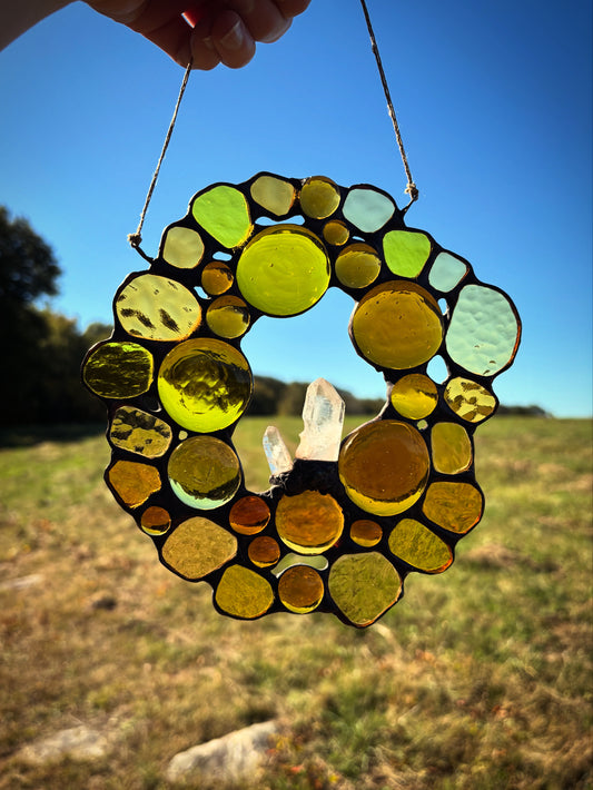 Stained glass circular hanging ornament with quartz crystals and a blue sky and field background.