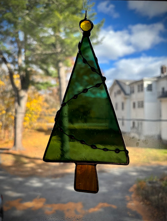Stained glass Christmas tree decoration with a house and trees in the background.