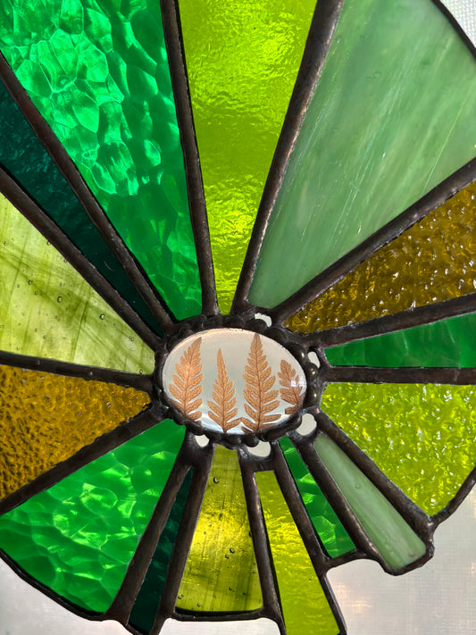 Stained glass panel with green and yellow colors and a central emblem with pressed ferns.