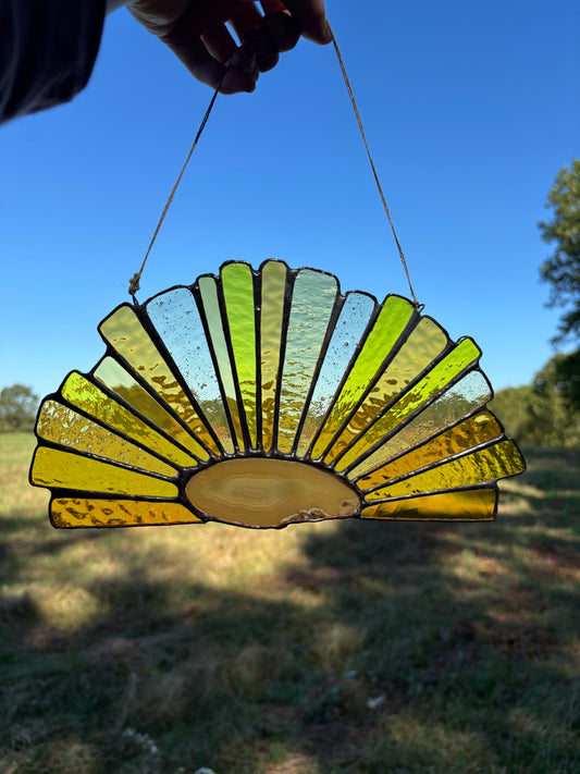 Decorative stained glass with an agate slice hanging outdoors against a blue sky.