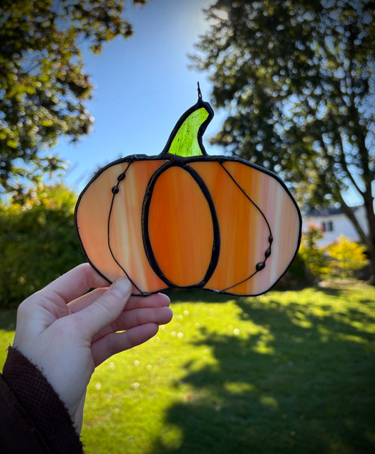 Stained glass pumpkin held by a hand with a garden background.